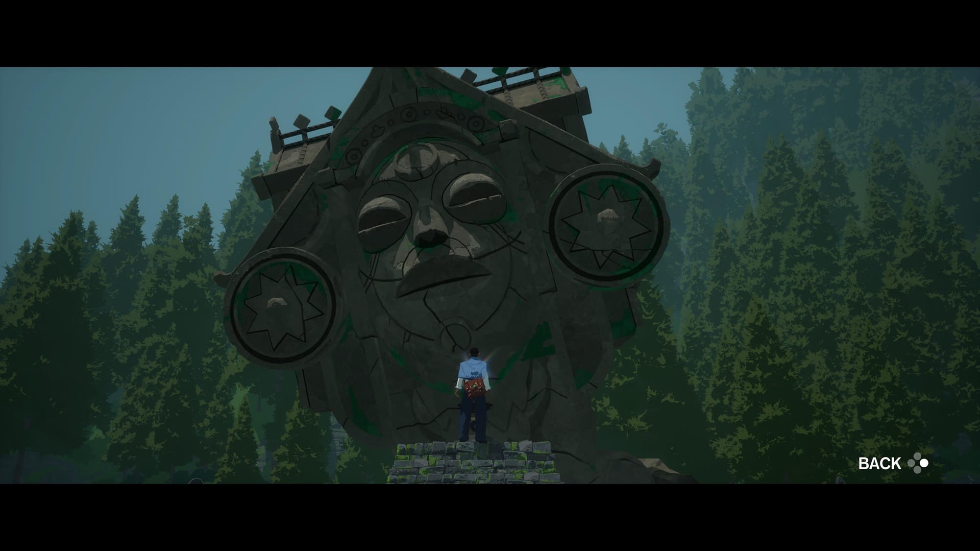 Main character is shown from the back on the background of a giant stone monument of the local god in the middle of the forest.